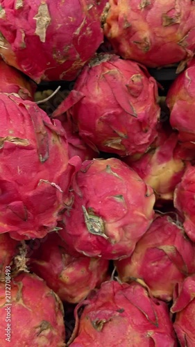 Vertical Video of Hand gently touches a vibrant pink dragon fruit. Fuzzy, scaley skin covers the round, sweet fruit. Bright red hues contrast with soft yellow undertones. The hand suggests a fresh, tr