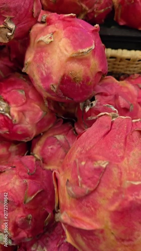 Vertical Video of Hand gently touches a vibrant pink dragon fruit. Fuzzy, scaley skin covers the round, sweet fruit. Bright red hues contrast with soft yellow undertones. The hand suggests a fresh, tr
