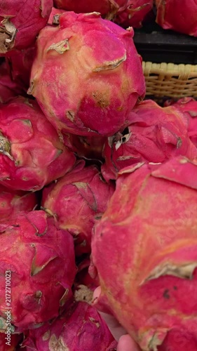 Vertical Video of Hand gently touches a vibrant pink dragon fruit. Fuzzy, scaley skin covers the round, sweet fruit. Bright red hues contrast with soft yellow undertones. The hand suggests a fresh, tr
