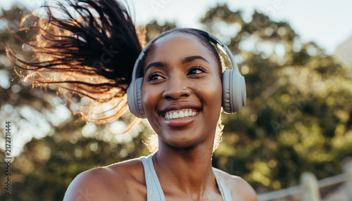 Young woman smiling joyfully while running outdoors in athletic wear on sunny day