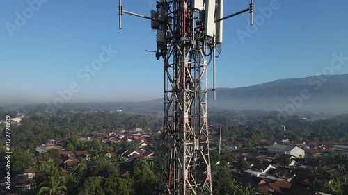 Aerial View of Several Radio Masts and Antennas Mounted on a Large Telecommunication Tower During Morning Against a Clear Blue Sky and Mountain Landscape in the Distance in Karanglewas, Indonesia.