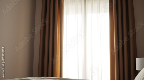 Bright sunlight streaming through sheer white curtains and brown drapes in a modern bedroom interior.