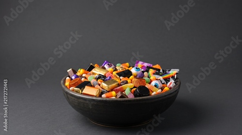 A full bowl of assorted Halloween candy including candy corn, chocolates, gummy candies, and eye candies on a dark background