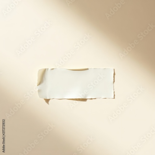 A single piece of torn white paper positioned centrally on a neutral beige background with soft natural lighting and copy space.