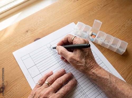 Elderly persons hand writing on paper with pill organizer nearby.