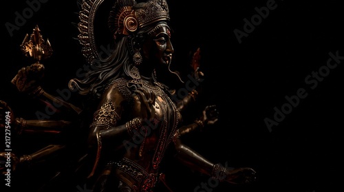 Elegant dark bronze goddess statue with intricate headdress and ornate jewelry in dramatic lighting with illuminated striking side lighting against deep black background