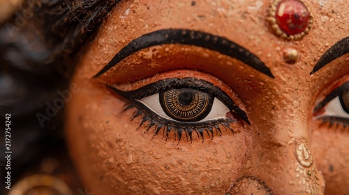 Close up of intricately hand painted terracotta deity eye with ornate adornments with richly textured surface under soft lighting eyeliner golden embellishments