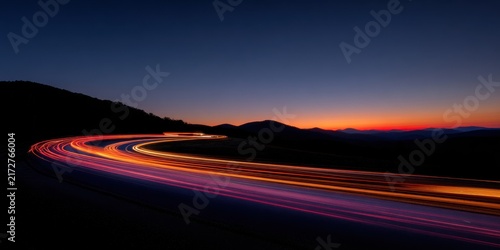 A winding road features blurred red car light trails under a dramatic twilight sky over mountain silhouettes. This represents travel, motion, and logistics.