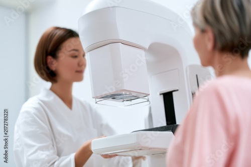 Medical staff performs a mammogram on a patient in a clinic setting during daylight hours
