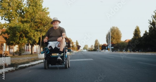 Front view of a senior man driving an electric wheelchair along a city road, showing independent mobility, confidence and active everyday life outdoors.