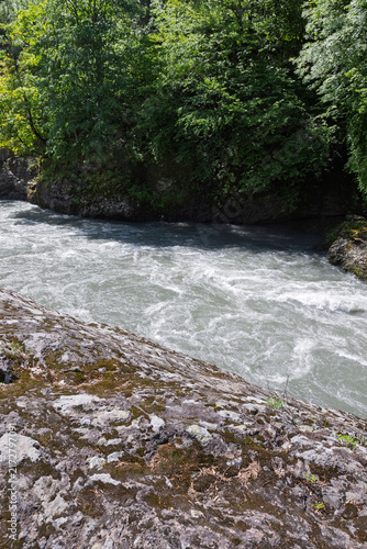 The riverbank zone in mountainous terrain, the rocky soil bordering the riverbed, with vegetation along the banks.