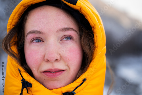 Fotografía Emotional close-up portrait of a female mountaineer in a yellow down jacket looking into the distance during a winter mountain expedition