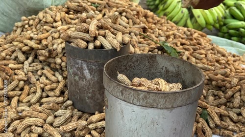Traditional metal volume measuring cans (liter cups) filled with raw peanuts, highlighting traditional trade measurement methods at an Asian market.