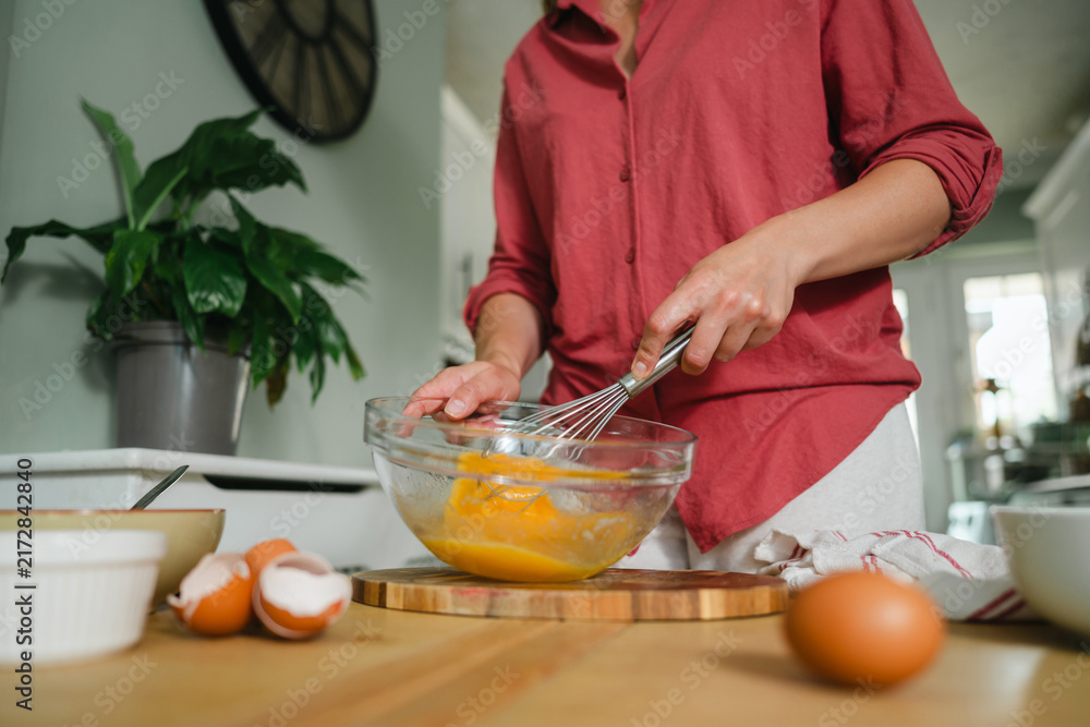 Naklejka premium Woman whisking eggs in a glass bowl in kitchen, cooking at home
