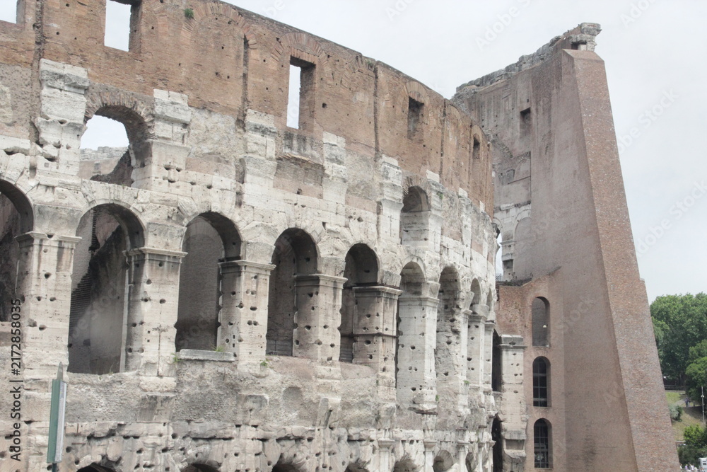 Obraz premium Side angle closeup of the Roman Colosseum displaying stone arches alongside its iconic brick reinforcement wall.