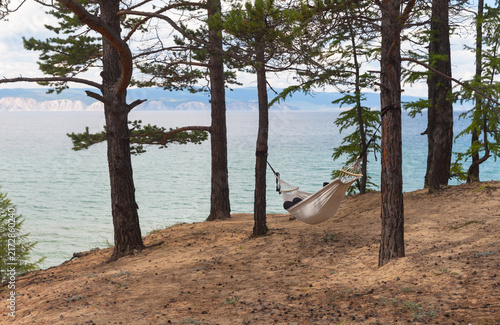 Lake Baikal. The coast of Olkhon Island. A tourist relaxes on the shore of the Small Sea and swings in a hammock on a summer day. Outdoor recreation