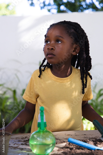 African American female child wearing yellow tee tending soil at garden table with blue trowel