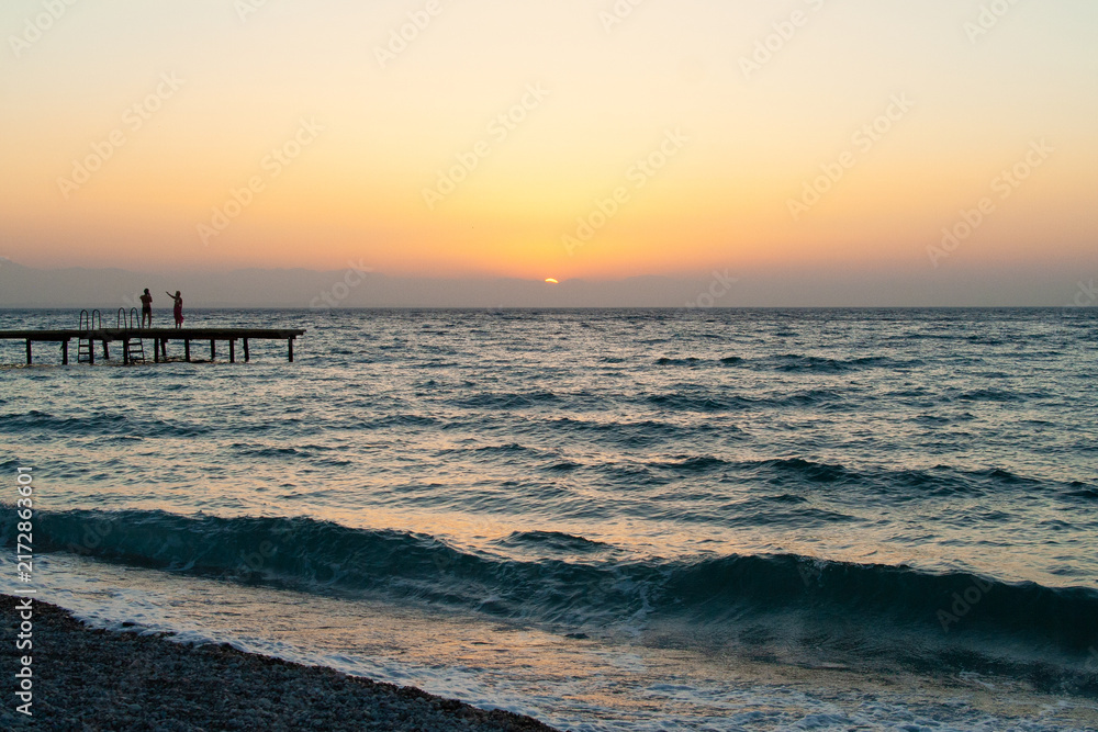 Fototapeta premium silhouette of people walking along the sea beach pier at sunset