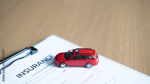 Obraz na płótnie Red model car on auto insurance form and clipboard on wooden desk, representing vehicle insurance, policy, coverage and protection with copy space
