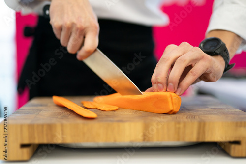 Canvas Print Chef slicing a fresh carrot on a wooden cutting board
