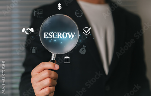 A businessman in a suit holding a magnifying glass emphasizes escrow assets held as collateral with a third party finance, security, and partnership, symbolizing secure transactions and trust.