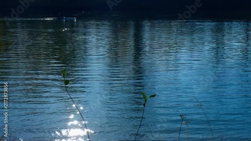 Person kayaking on a calm lake with sun reflection. Kayaker paddling on a serene lake, with the bright morning sun reflecting on the rippling blue water surface, creating a peaceful atmosphere