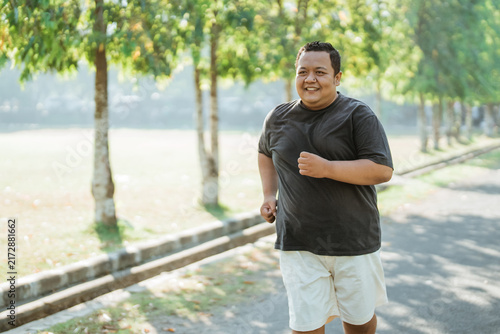 portrait of an overweight Asian man jogging in the park in the morning with copyspace