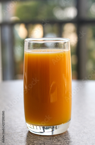 Fotografie Glass of fresh orange juice standing on a surface with a blurred background