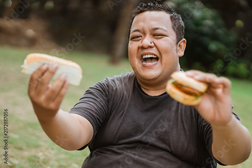 overweight young man happy while eating a lot of bread in his hand with an outdoor background