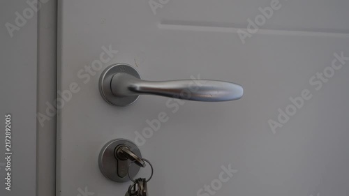 Man’s hand turning silver door handle with key in lock on white door