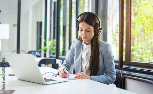 Young call center operator taking notes during customer support phone call