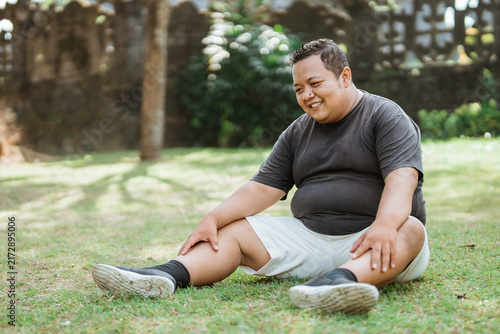 Asian fat man wearing sportswear sits leisurely below while in an outdoor background