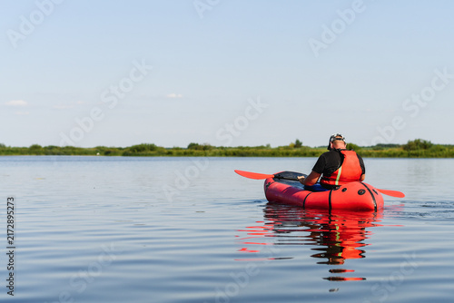 Man packrafting on calm open lake under clear blue sky during outdoor adventure trip.