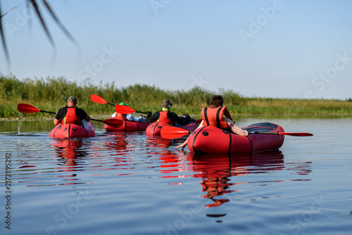 Group of people packrafting on calm river on sunny day during an outdoor adventure trip.