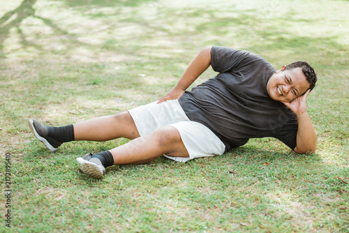 fat man wearing workout clothes lays back and relaxes in an outdoor background