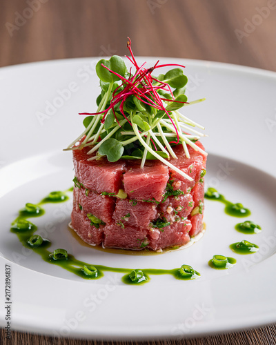 Tuna Tartare Perfection A beautifully plated tower of fresh tuna tartare, meticulously diced and seasoned, adorned with vibrant microgreens and a drizzle of green herb oil.