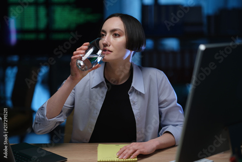 Obraz na płótnie Businesswoman drinks water from clear glass while sitting at office desk