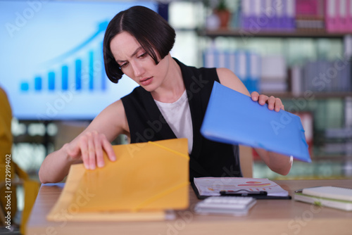 Foto Female manager searches carefully for missing document on crowded desk