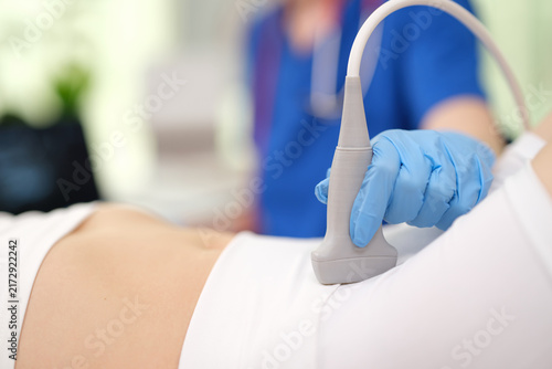 Fotografía medical professional performing ultrasound examination on patient's abdomen in clinical setting with plastic ultrasound probe and white gloves, close-up view highlighting professional care