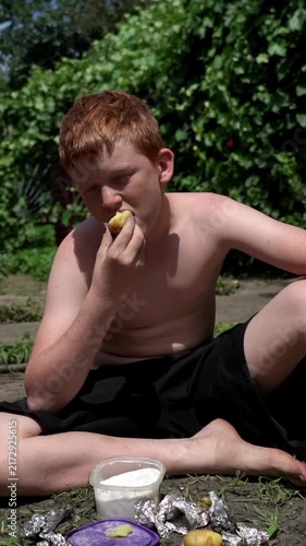 The guy is sitting on the ground and eating potatoes baked in foil over charcoal.