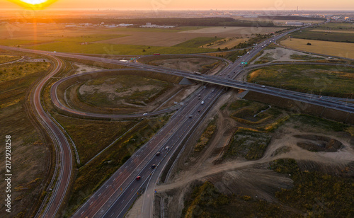Obraz na płótnie Aerial view of Bucharest A0 ring road motorway interchange at golden sunrise, showcasing modern highway infrastructure, traffic, and glowing horizon in Romania