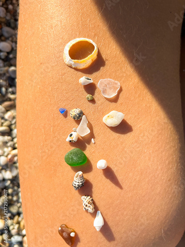 Vertical top view of small sea shells and polished beach sea glass pieces arranged on a woman's sun tanned skin