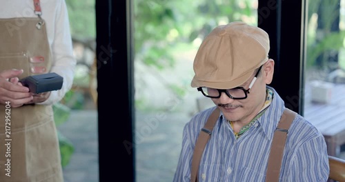 Senior asian man looking toward waiter with payment device after reunion lunch in restaurant, preparing checkout, relaxed dining moment, casual bill payment, hospitality interaction