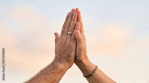 Close up of two hands giving a high five against a soft neutral background, symbolizing teamwork, partnership, success, support and celebration.