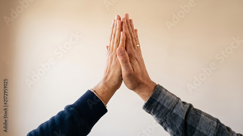 Close up of two people giving a high five against a warm background, representing teamwork, success, partnership, encouragement and positive collaboration.