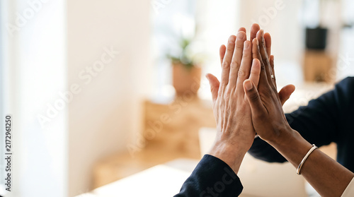 Close up of two hands giving a high five on a clean neutral background, symbolizing teamwork, cooperation, partnership, support, success and unity.