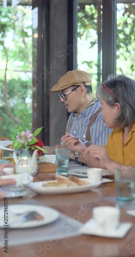 Senior asian retiree man shares brunch conversation with close friend at restaurant table, smiling during reunion meal, warm social bonding, supportive talk, later life connection, Vertical frame