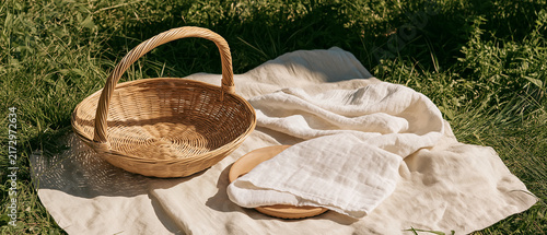 Picnic Basket in Summer Meadow: A charming woven picnic basket sits on a neutral blanket spread across a sun-drenched green meadow, evoking a sense of leisurely outdoor enjoyment and simple pleasures.