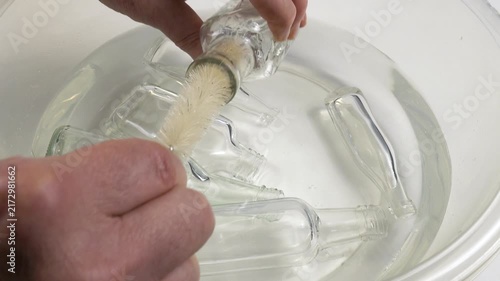 Human washing small glass bottle with bottle brush in a bowl with water, household chores