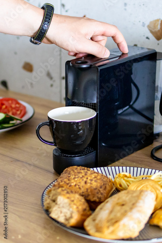 Фотография Close up of hand pressing button on coffee machine beside fresh pastries for breakfast